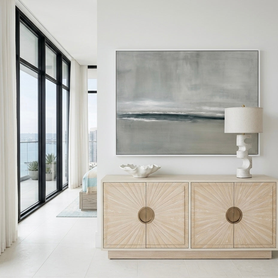 Modern interior with a light wood console table, abstract painting, and lamp.