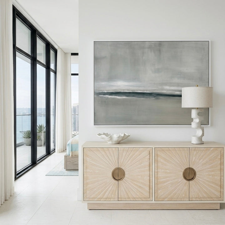 Modern interior with a light wood console table, abstract painting, and lamp.